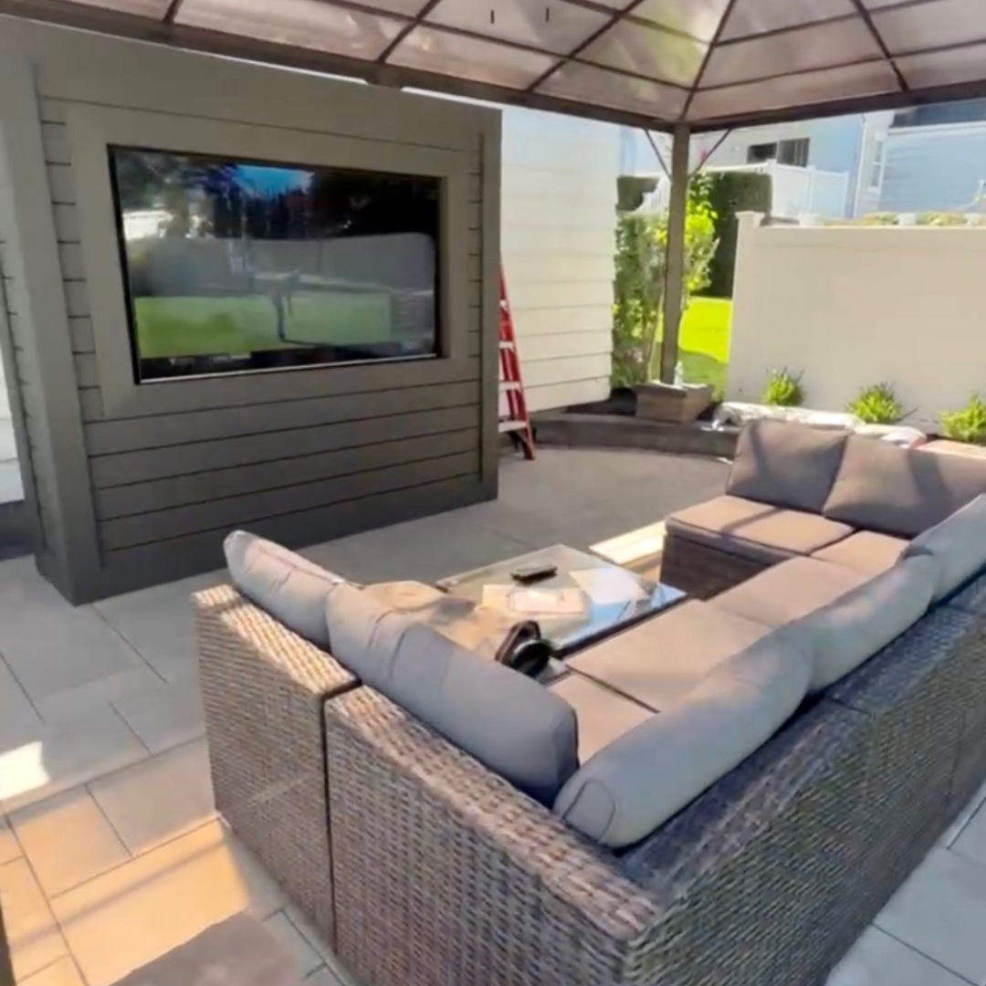 Outdoor living area with a pergola, TV, and comfortable seating designed by Safe Way Outdoor Services